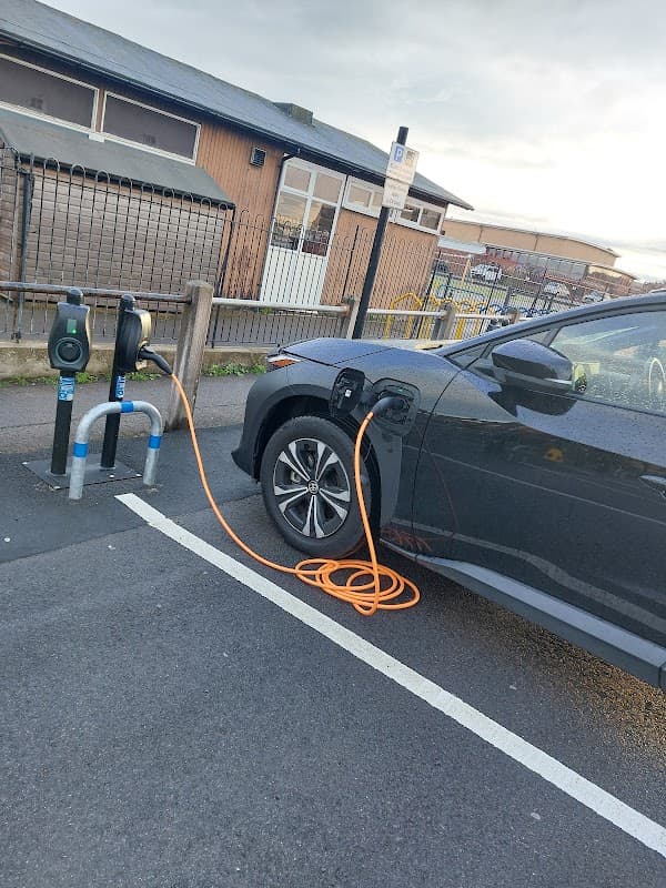 Connected Kerb charging station with an electric vehicle plugged in, orange charging cable visible, in a parking area.