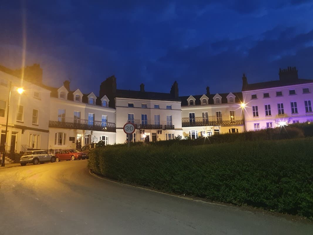 Haven Guesthouse Whitby at night, featuring illuminated buildings, parked cars, and a curved road lined with hedges.