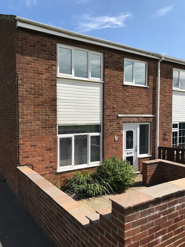 Brick house with white windows and a front garden, located in Whitby, North Yorkshire. Clear blue sky above.