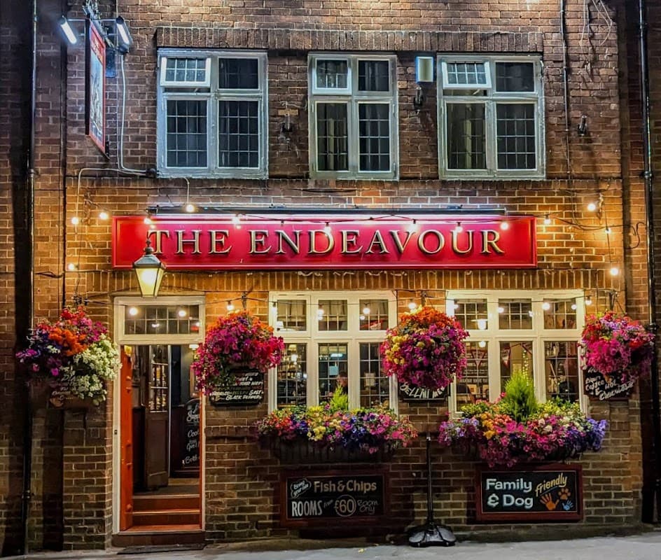 The Endeavour bar features a brick facade, vibrant flower baskets, and illuminated signage in Whitby, Yorkshire.
