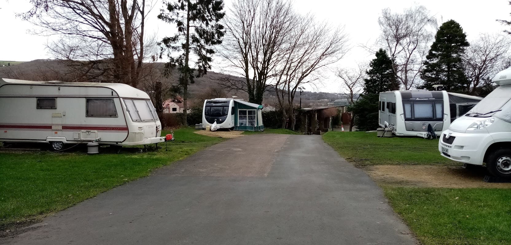 Caravan park with parked caravans, a pathway, and trees in a rural setting at Elland Hall Farm, Exley, Yorkshire.