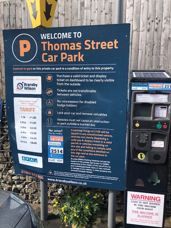 Welcome sign for Thomas Street Car Park with parking tariff details and a pay station in Exley, Yorkshire.