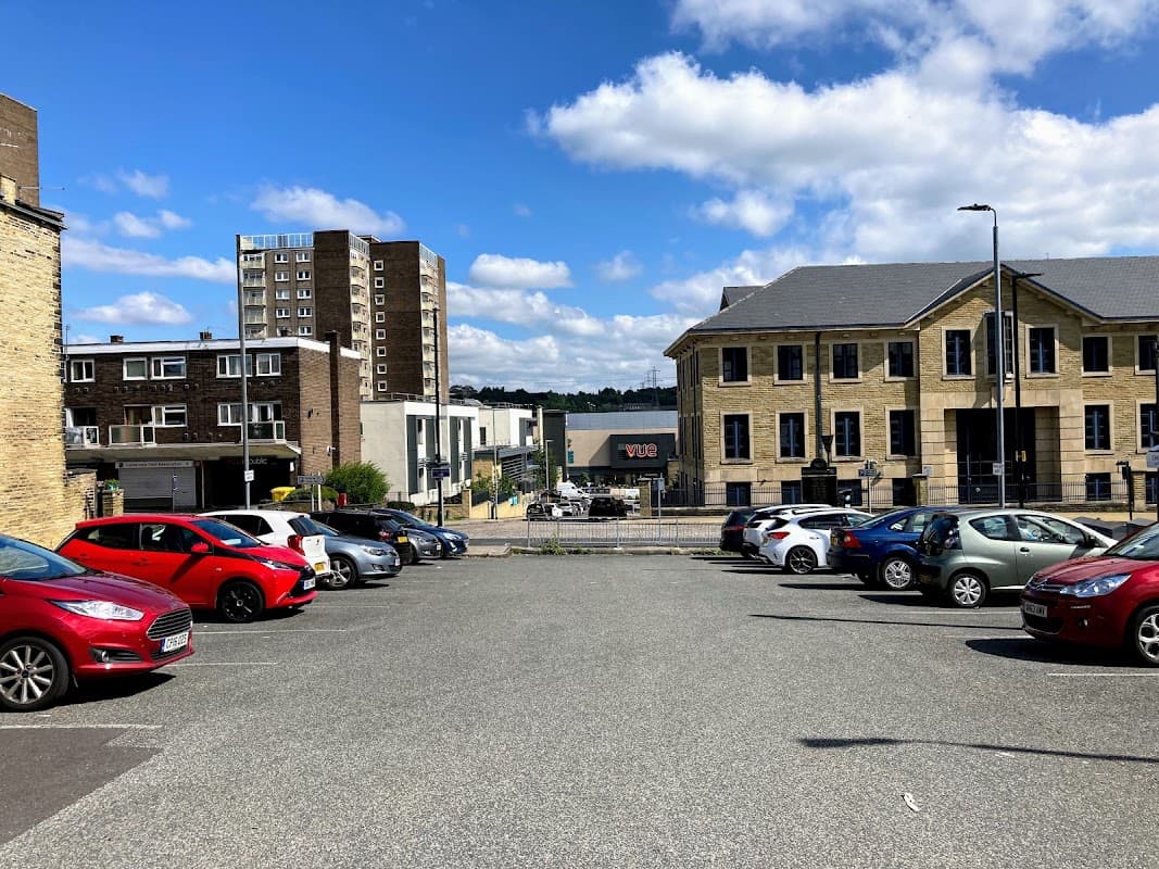 Free parking area with various cars, buildings in the background, and a clear blue sky with clouds.