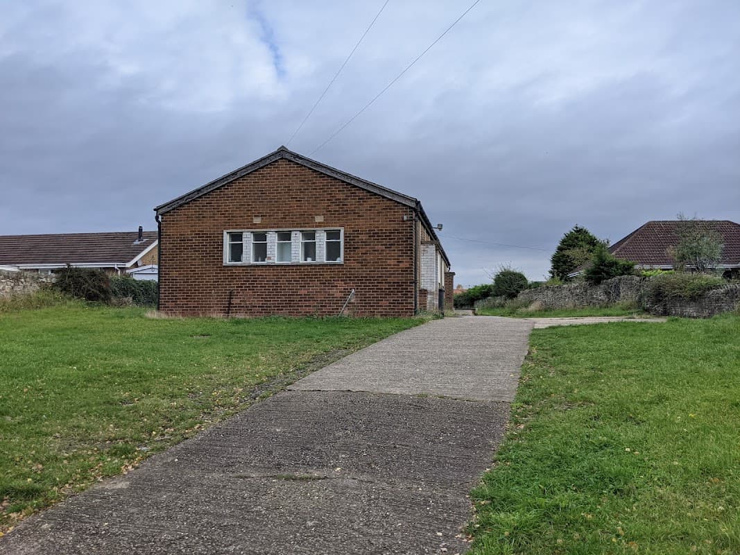 Fairburn Old Church Hall, a brick building with multiple windows, set on a grassy area with a concrete path leading up to it.