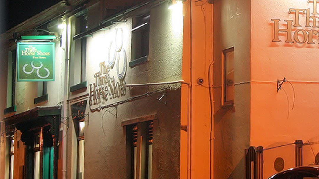 Three Horse Shoes bar exterior with illuminated signs, featuring a green and white color scheme in Fairburn, North Yorkshire.