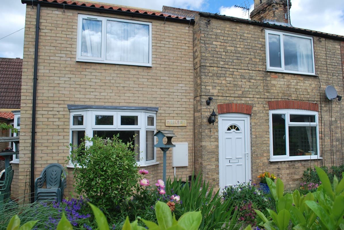 Charming brick building with white windows, a front door, and colorful garden plants in Fangfoss, Yorkshire.