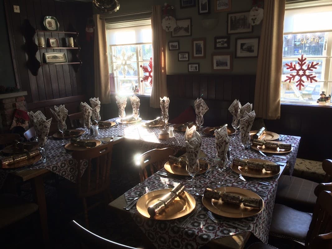 Tables set for a festive meal with gold plates, folded napkins, and Christmas decorations in a cozy pub interior.