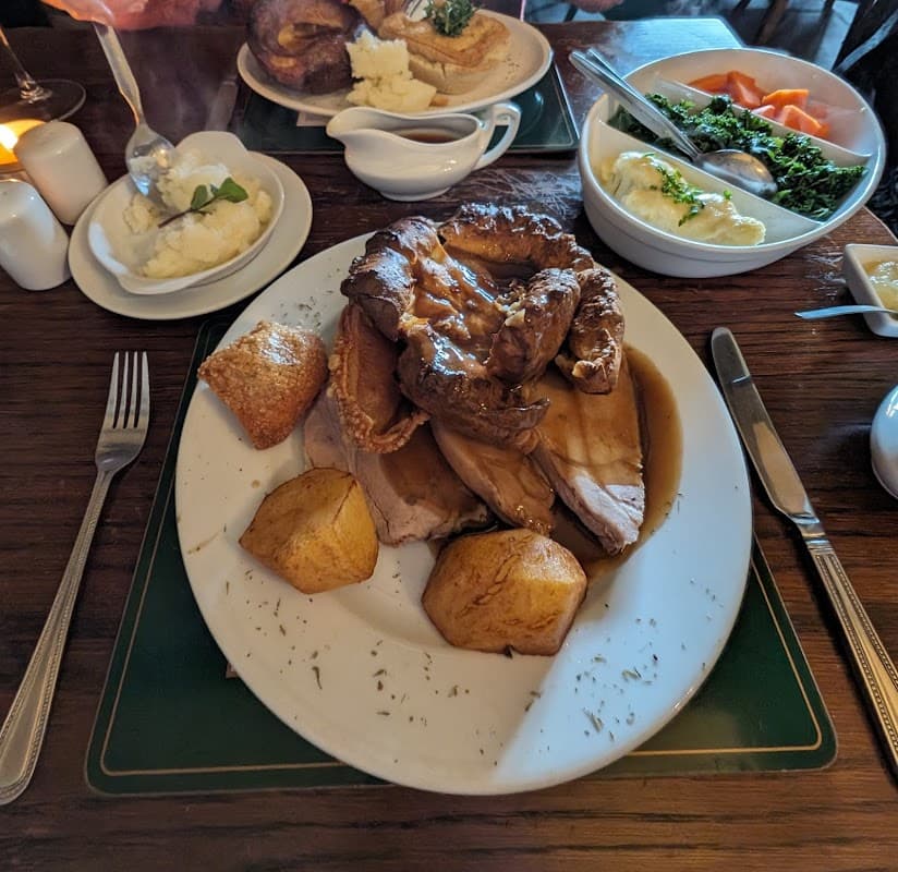 A plate of roast meat with Yorkshire pudding, roast potatoes, and gravy, surrounded by side dishes at a cozy pub table.