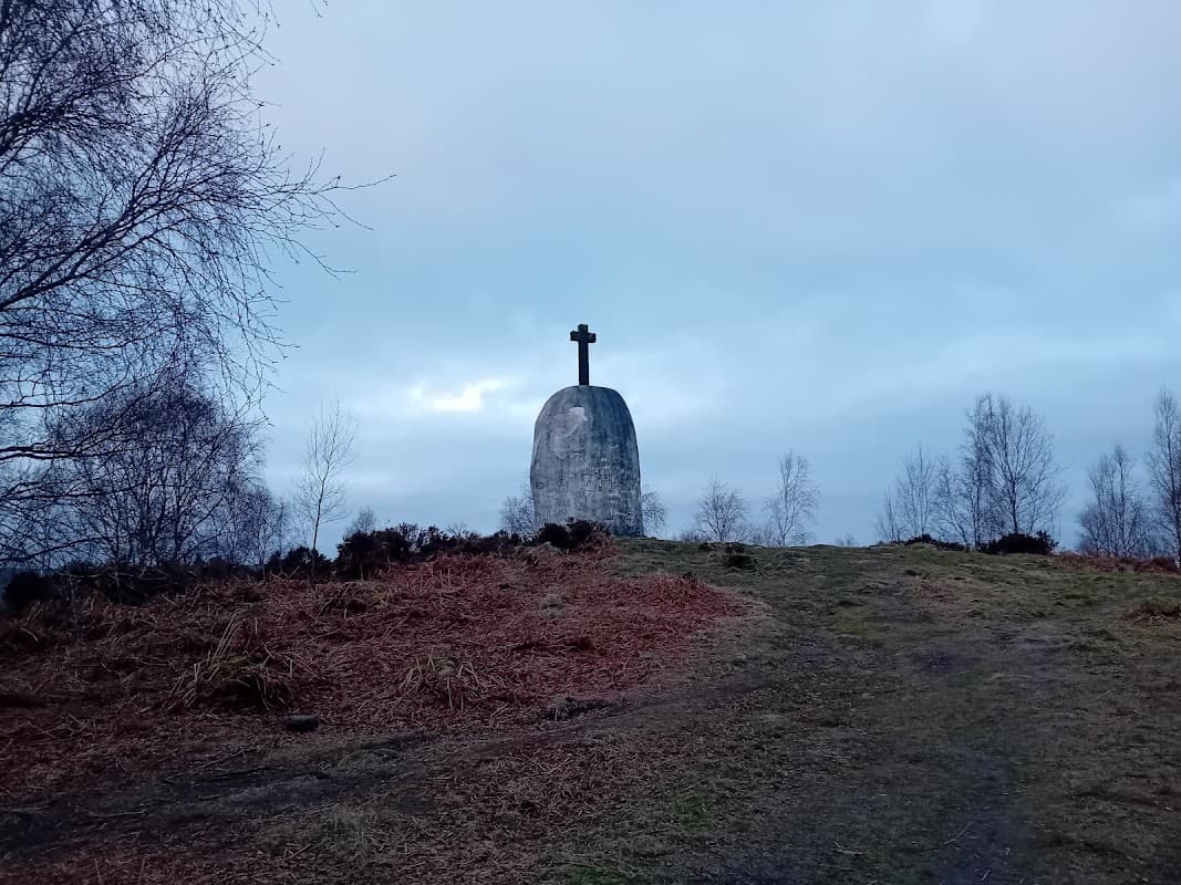 A large stone monument with a cross atop, surrounded by trees and a cloudy sky in Farnhill, Yorkshire.