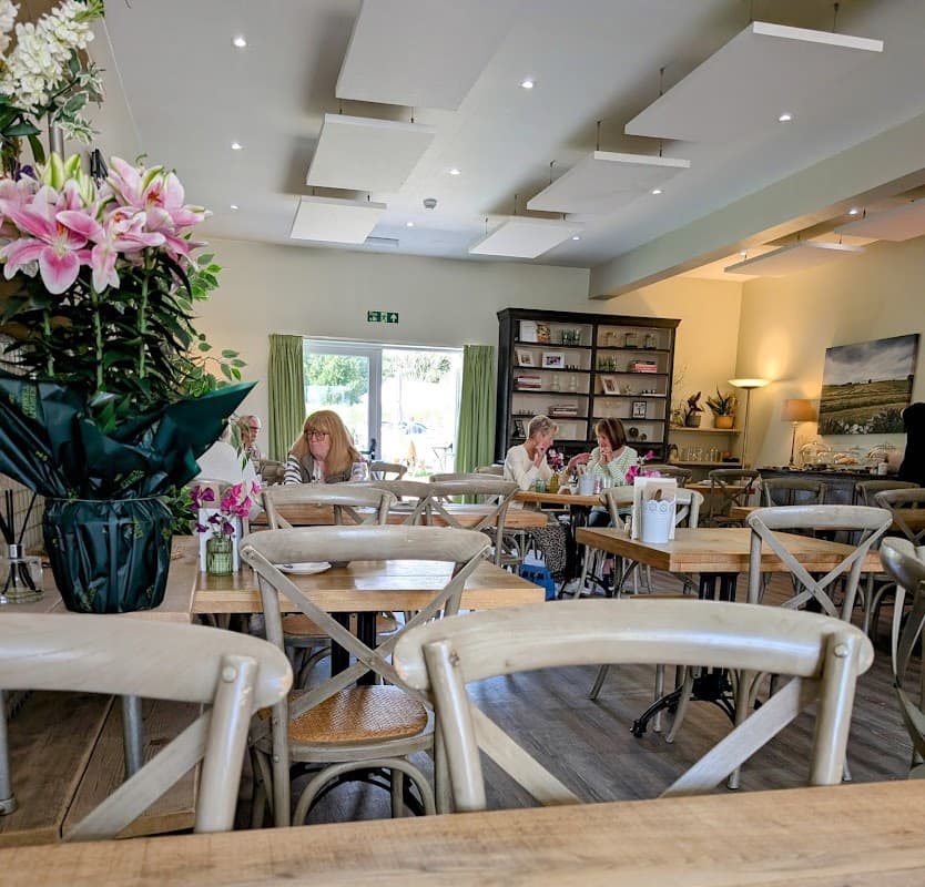 Bright café interior with wooden tables, floral arrangements, and patrons enjoying meals in a cozy atmosphere.