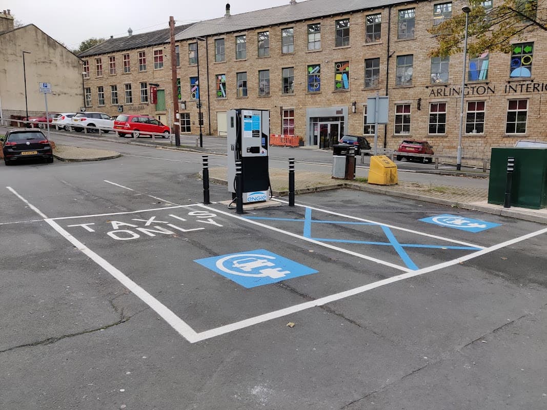 Free parking area with marked taxi spaces, electric vehicle charging station, and nearby brick buildings in Farsley.