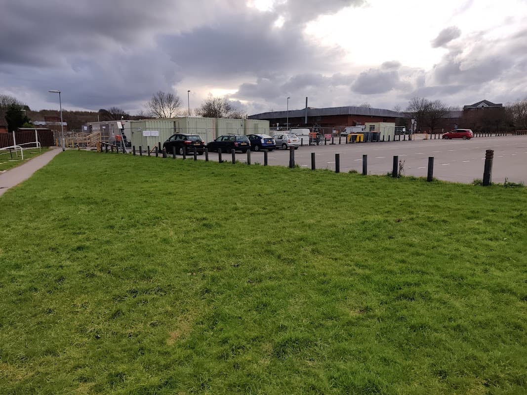 Grassy area in foreground with a car park in the background, featuring parked cars and overcast skies.