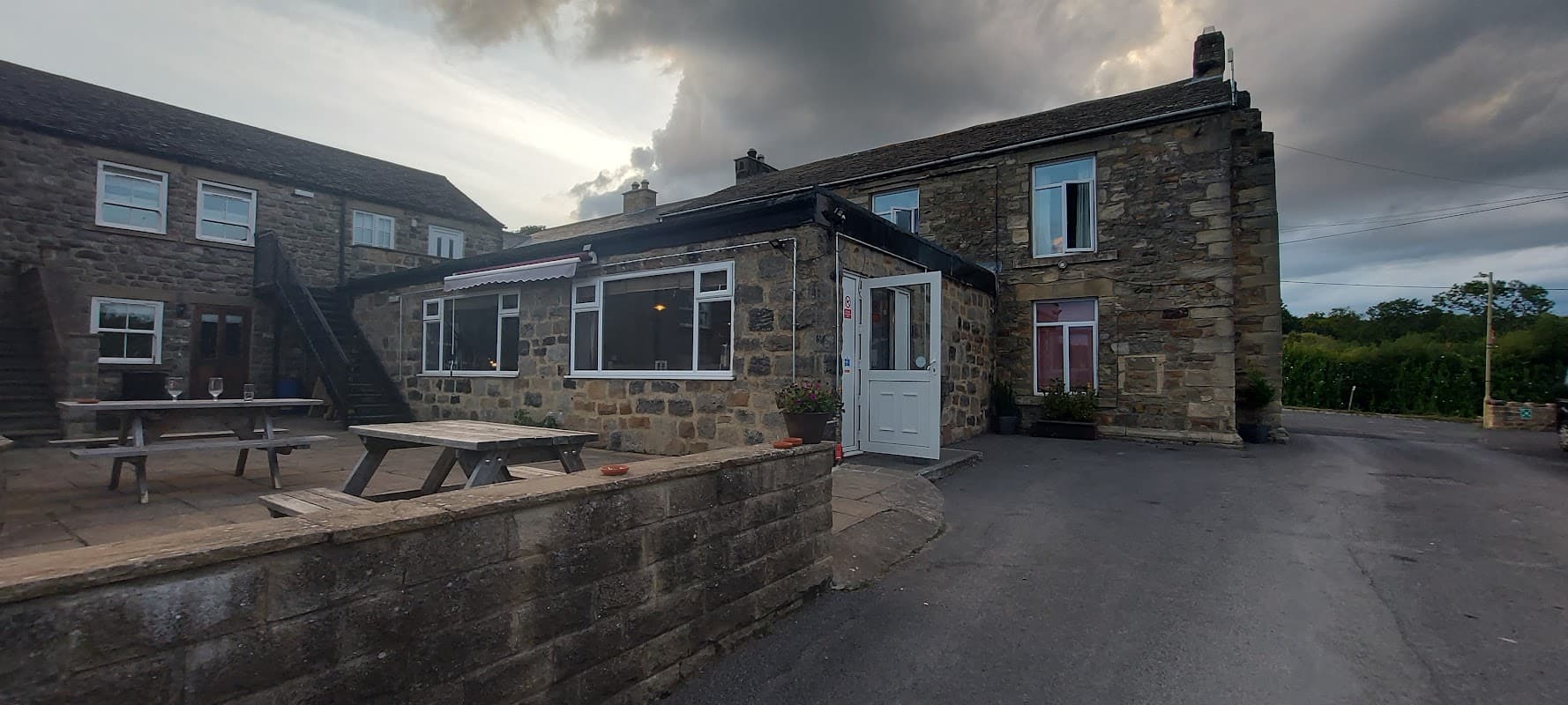 Stone building with large windows, wooden picnic tables, and a cloudy sky in Fearby, Yorkshire.