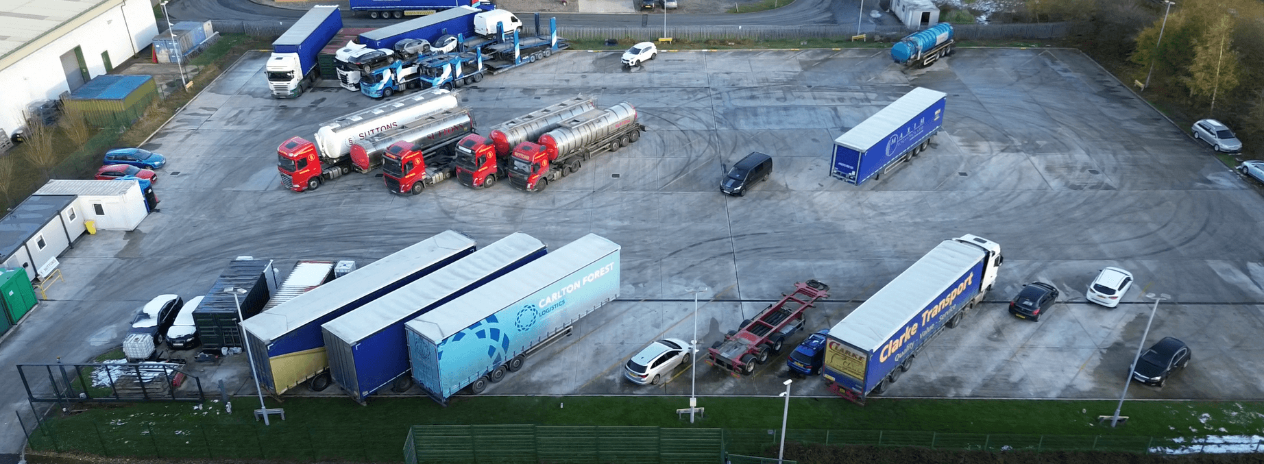 Aerial view of Onward Lorry Park with parked trucks, trailers, and a few cars on a large gravel lot.