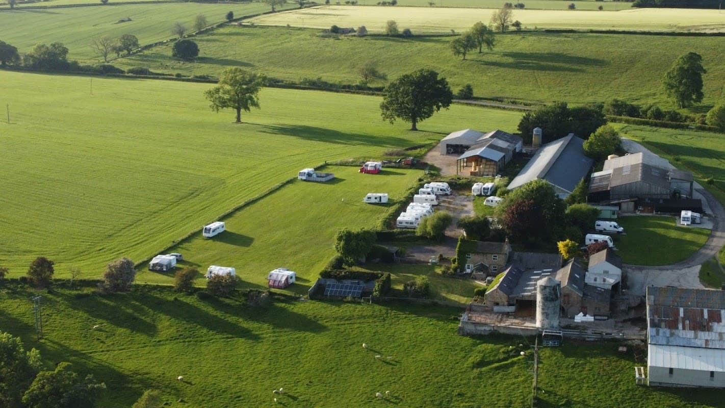 Aerial view of Unthank Farm, featuring fields, farm buildings, and parked caravans in a green landscape.