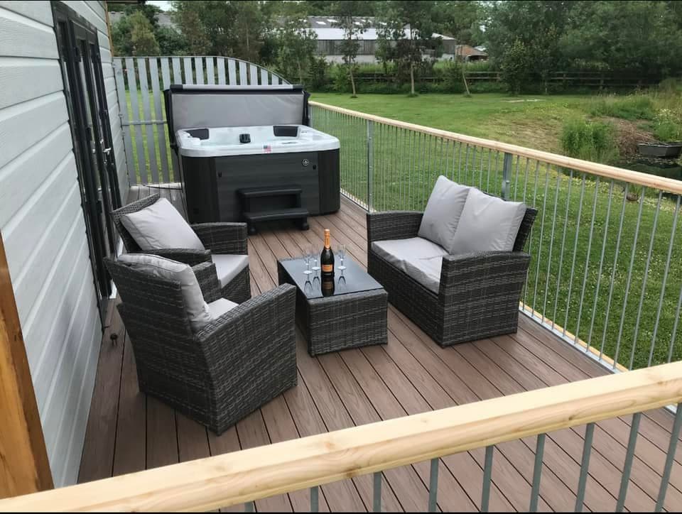 Cozy deck area with two chairs, a table, a hot tub, and a bottle of champagne, surrounded by greenery.
