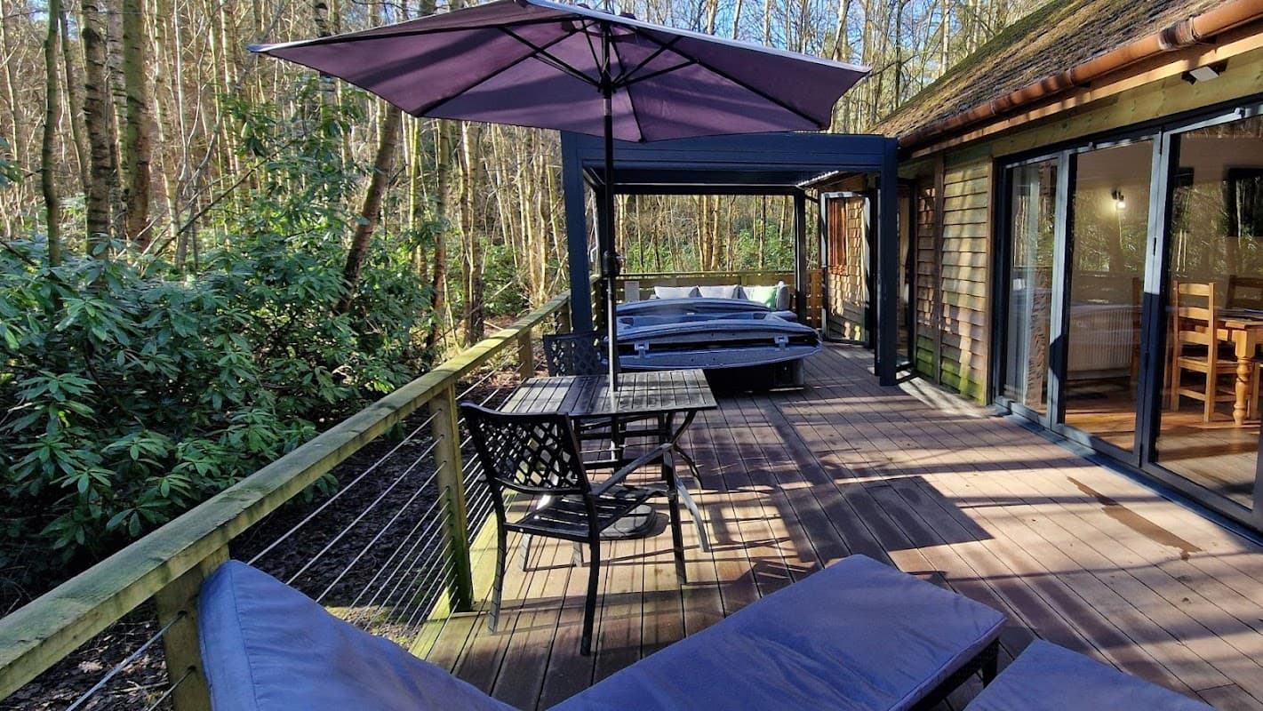 Cozy wooden deck with loungers, a dining table, and a hot tub surrounded by lush trees at Griffon Forest Holiday Lodges.