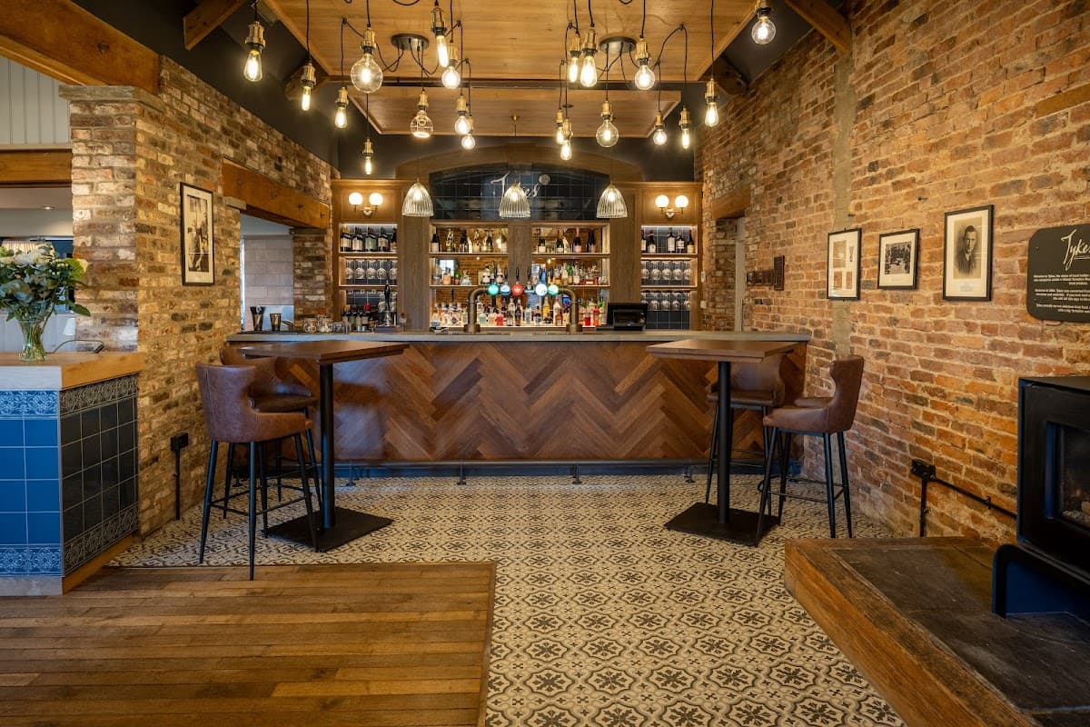 Stylish bar area with wooden flooring, exposed brick walls, and pendant lights, featuring high stools and a patterned tile floor.