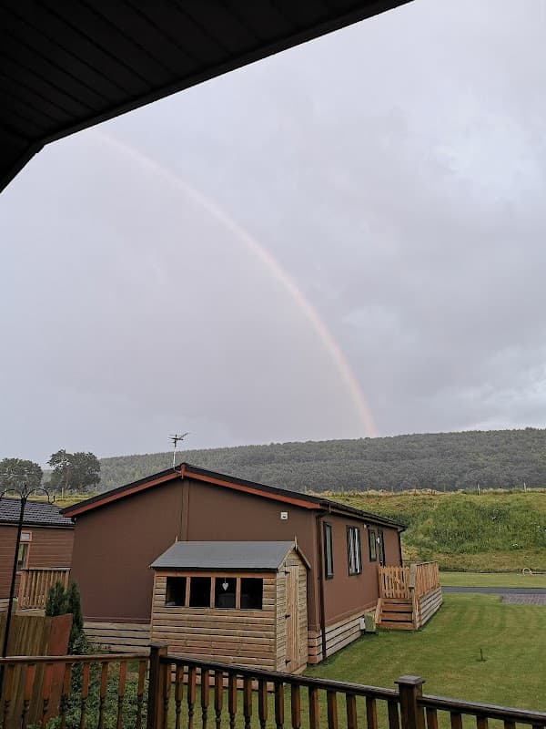 Luxury lodge with wooden exterior, surrounded by greenery and a rainbow arching over a distant hill in Flixton.