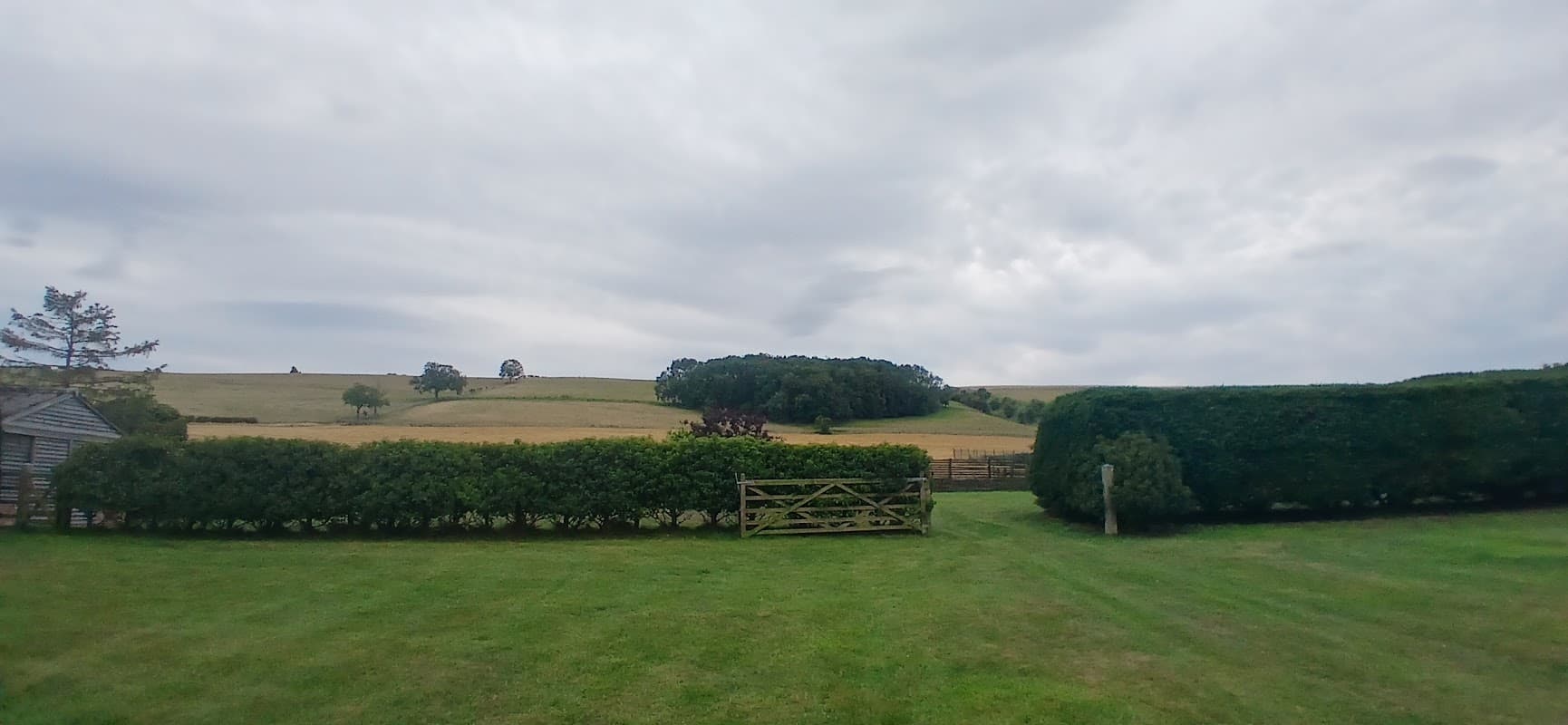 Lush green lawn with hedges and a wooden gate, overlooking rolling hills under a cloudy sky in North Yorkshire.