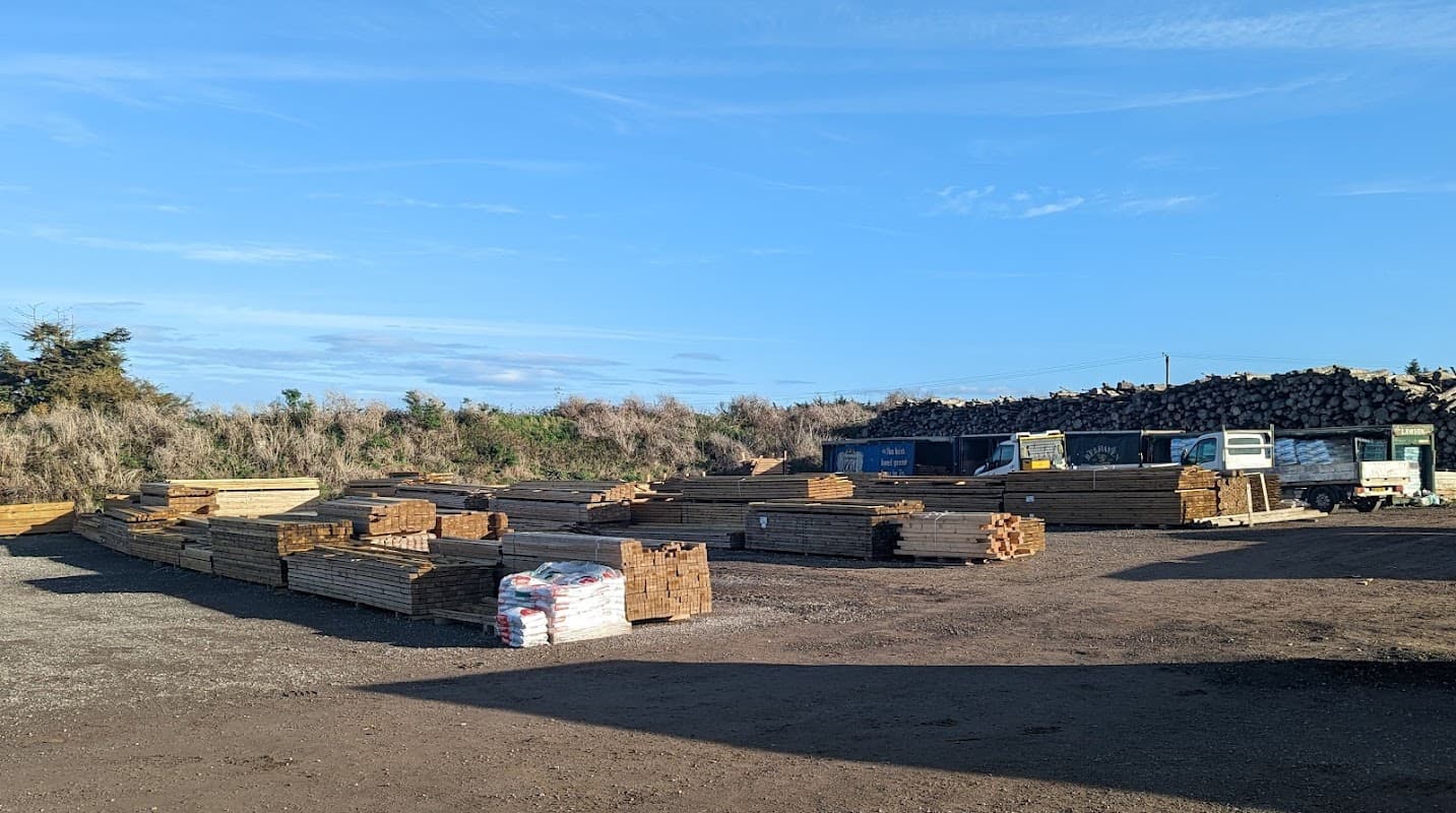 Wooden planks and stacks of timber are arranged in a sawmill yard under a clear blue sky.