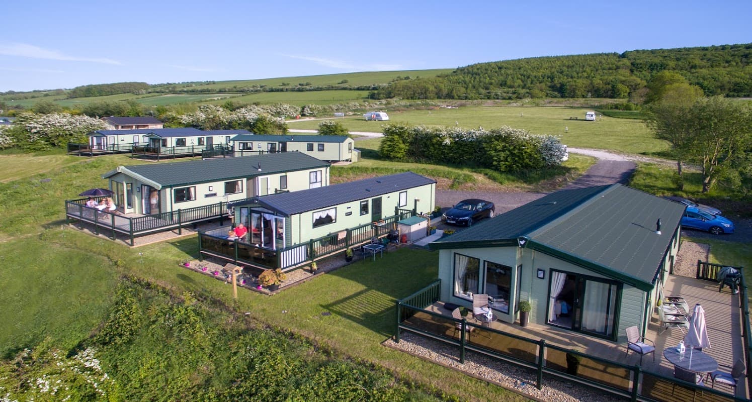 Scenic holiday park with modern lodges, green fields, and trees in Flixton, North Yorkshire. Clear blue sky above.