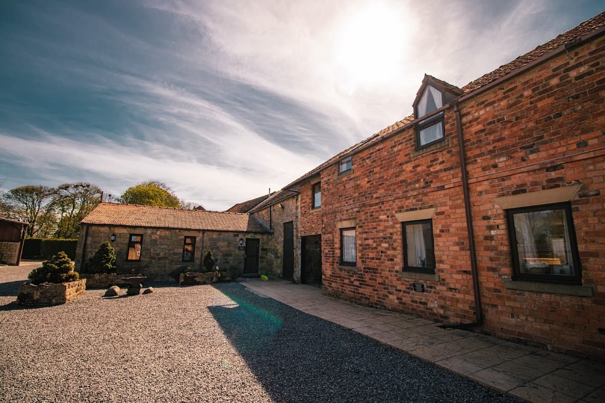 Red brick buildings with a gravel courtyard, surrounded by greenery and a bright sky in Folkton, Yorkshire.