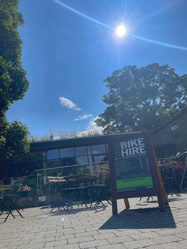 Sunny day at Dales Bike Centre with a bike hire sign and outdoor seating in front of a stone building.