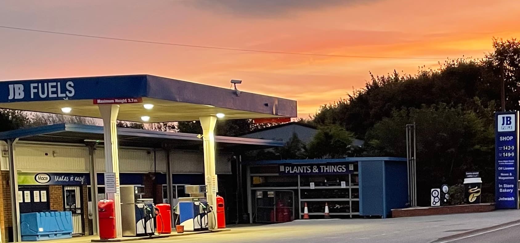 JB Fuels petrol station at dusk, featuring fuel pumps and a sign for "Plants & Things" with a colorful sunset backdrop.