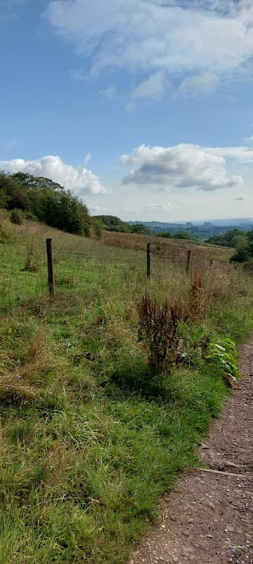 Scenic view of Porter Brook Trail with grassy hills, a blue sky, and distant landscape under fluffy clouds.