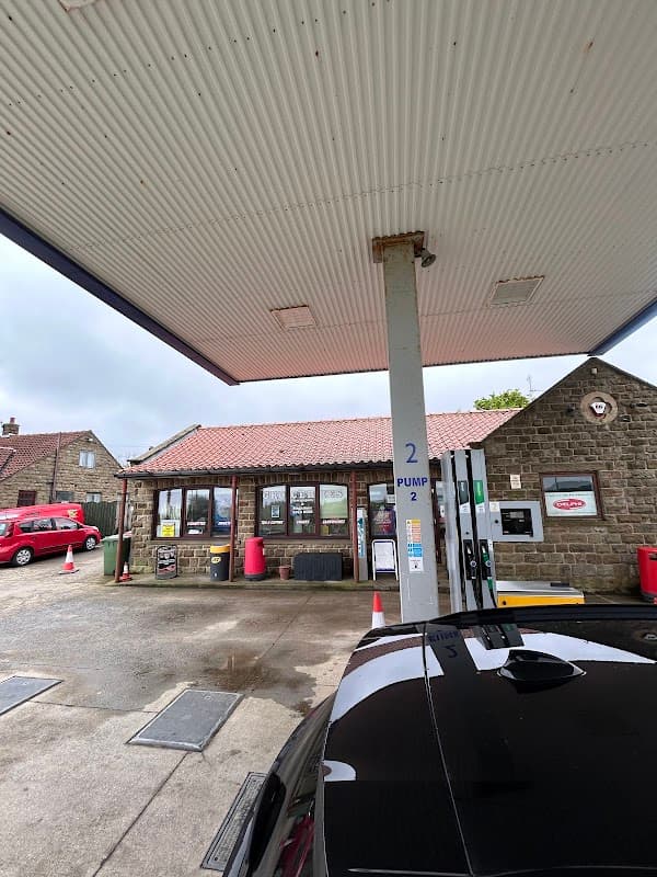 Fylingdales Service Station with stone exterior, fuel pumps, and red vehicles under a cloudy sky.