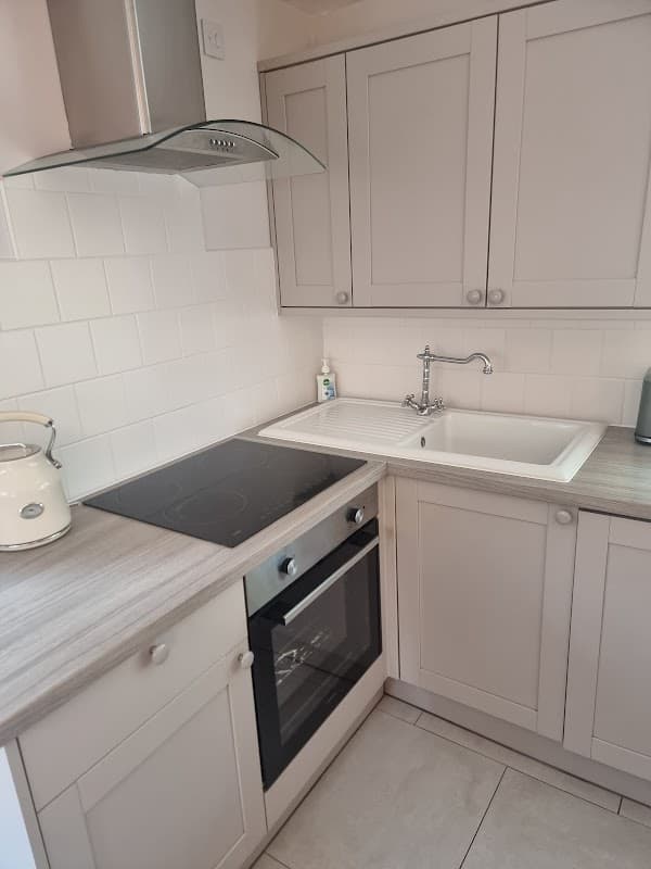 Modern kitchen with white cabinetry, sink, electric stove, and oven, featuring light-colored countertops and tiled floor.