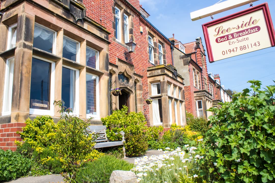 Charming brick hotel with large windows, lush garden, and a sign for "Lee-Side Bed & Breakfast" in Fylingthorpe.