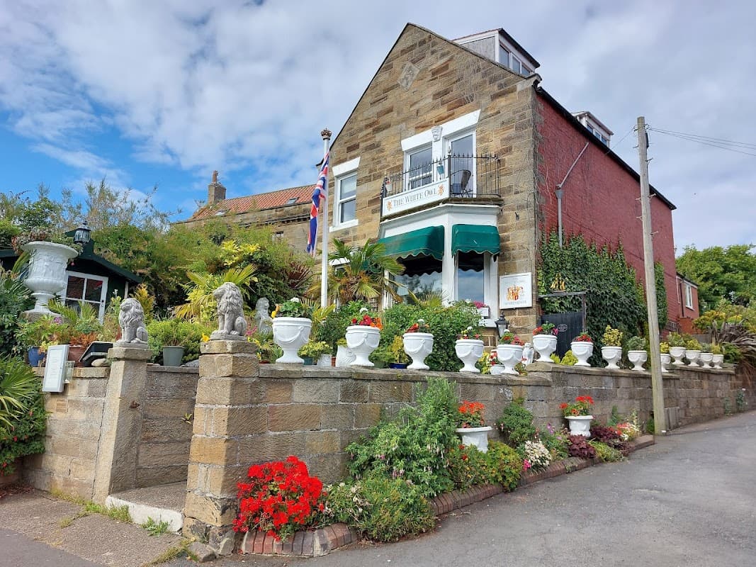 Charming hotel with stone facade, flower-filled planters, British flag, and lush greenery in Fylingthorpe, Yorkshire.