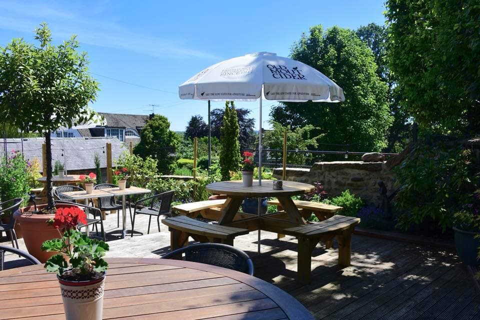 Sunny outdoor seating area at The Galphay Inn, featuring picnic tables, potted plants, and a large umbrella.