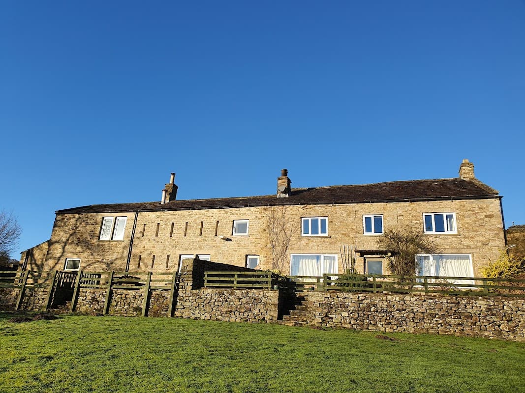 Stone farmhouse with multiple windows and a grassy foreground, set against a clear blue sky in Yorkshire.