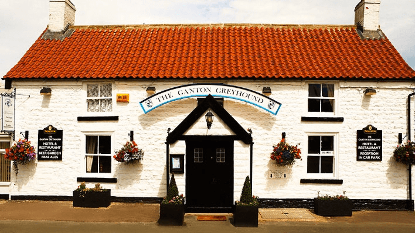 Charming white stone restaurant with a red-tiled roof, hanging flower baskets, and a welcoming entrance in Ganton, Yorkshire.