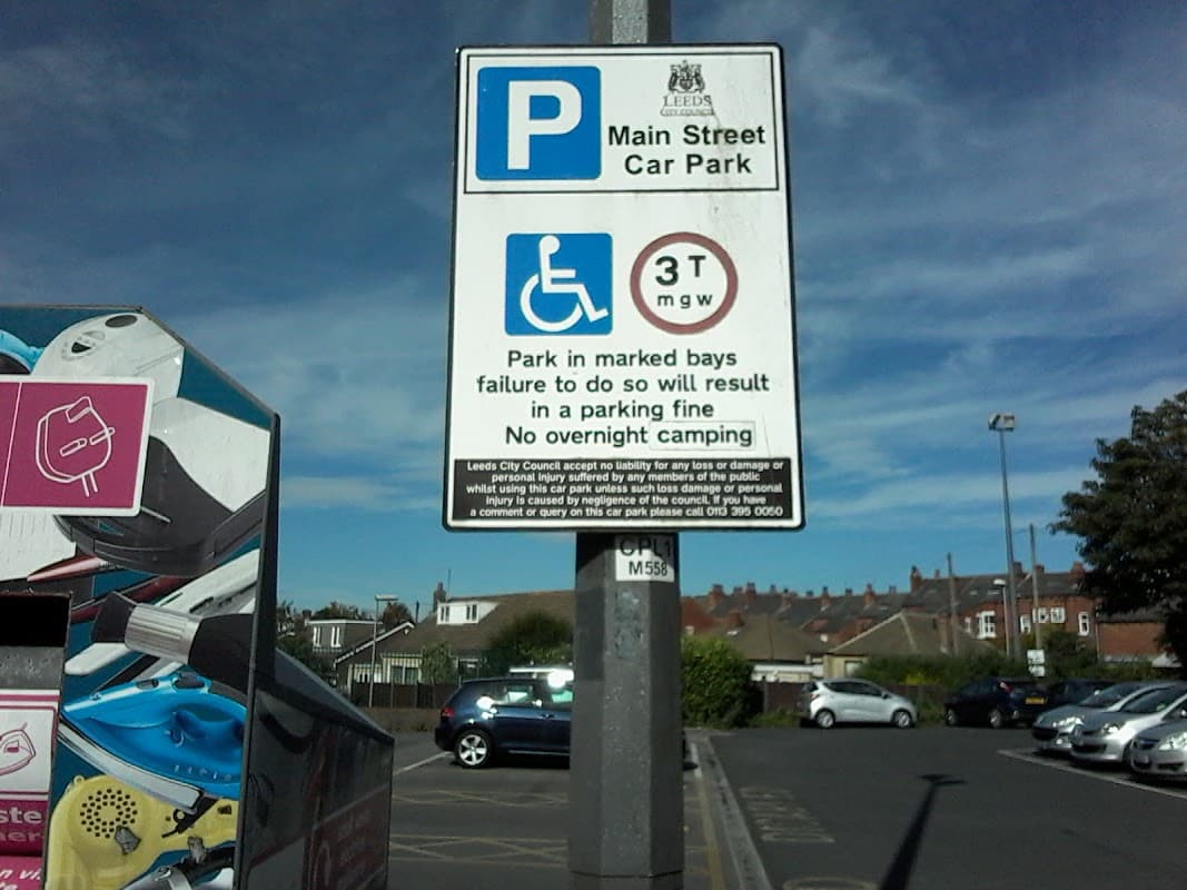 Main Street Car Park sign with parking regulations, blue sky, and cars in the background.