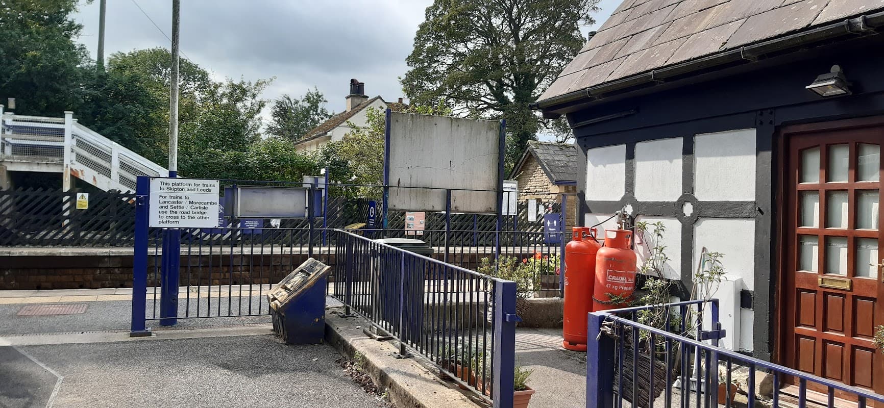 A quaint station building with blue and white accents, surrounded by greenery and a sign indicating Gargrave station.