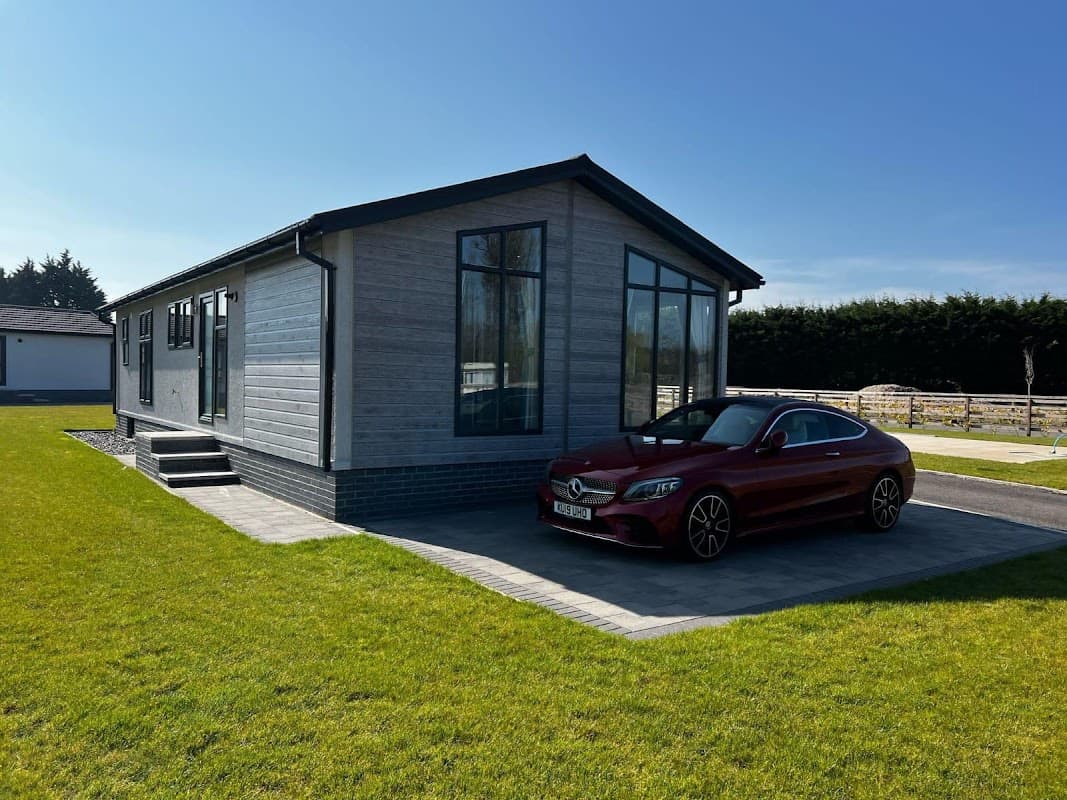 Modern hotel building with large windows, green lawn, and a red car parked in front under a clear blue sky.