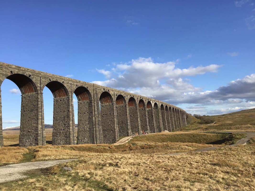 Historic stone viaduct with multiple arches, set against a blue sky and grassy landscape in Gearstones, Yorkshire.