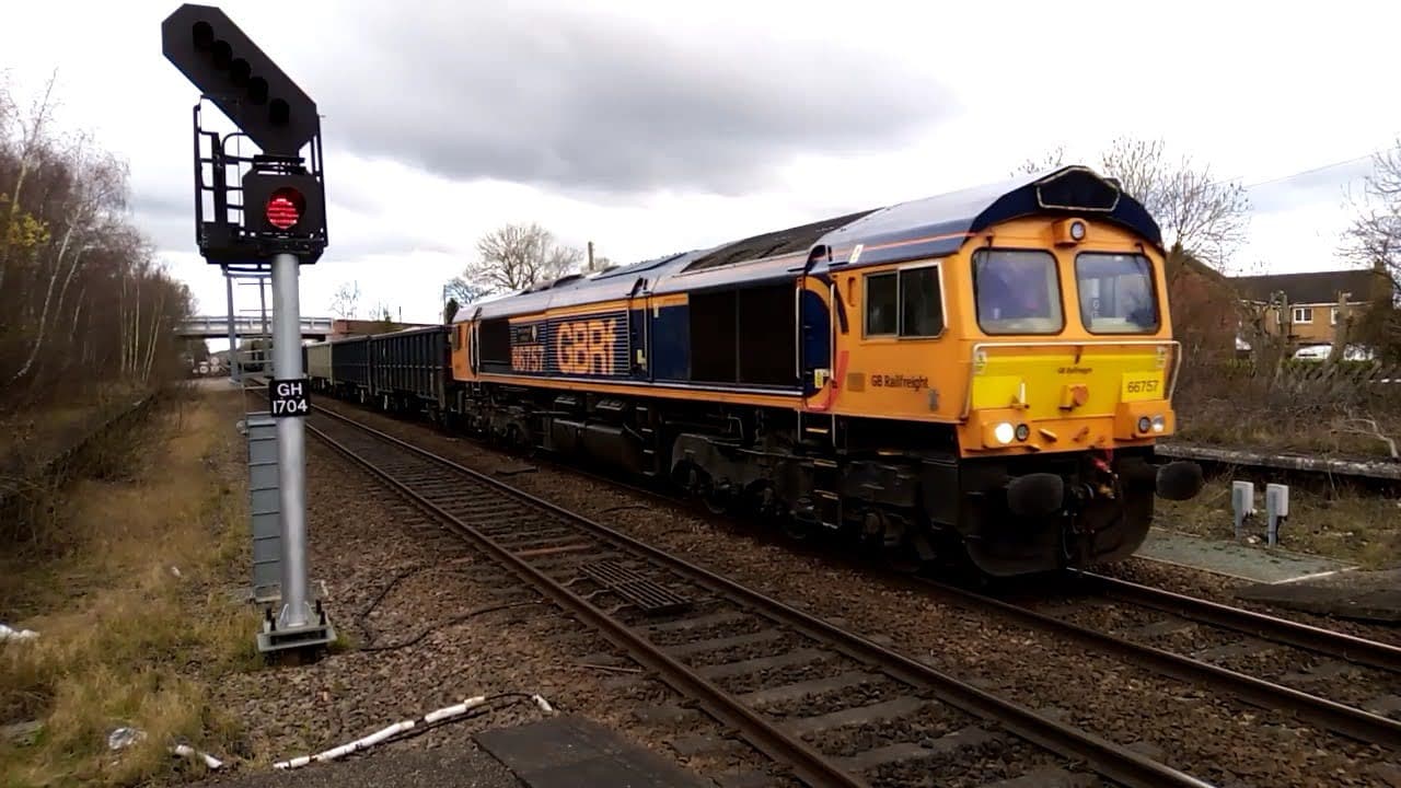 A freight train passes by a red signal at Gilberdyke station, surrounded by a rural landscape.