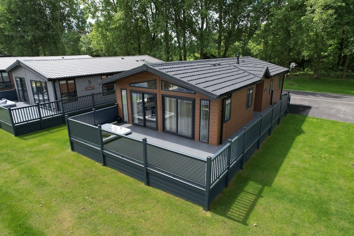 Modern lodge surrounded by greenery, featuring a spacious deck and privacy fencing in Wild Rose Country Park, Yorkshire.