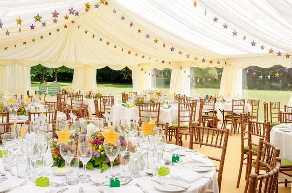 Elegant marquee decorated with colorful stars, featuring round tables set with floral centerpieces and glassware.