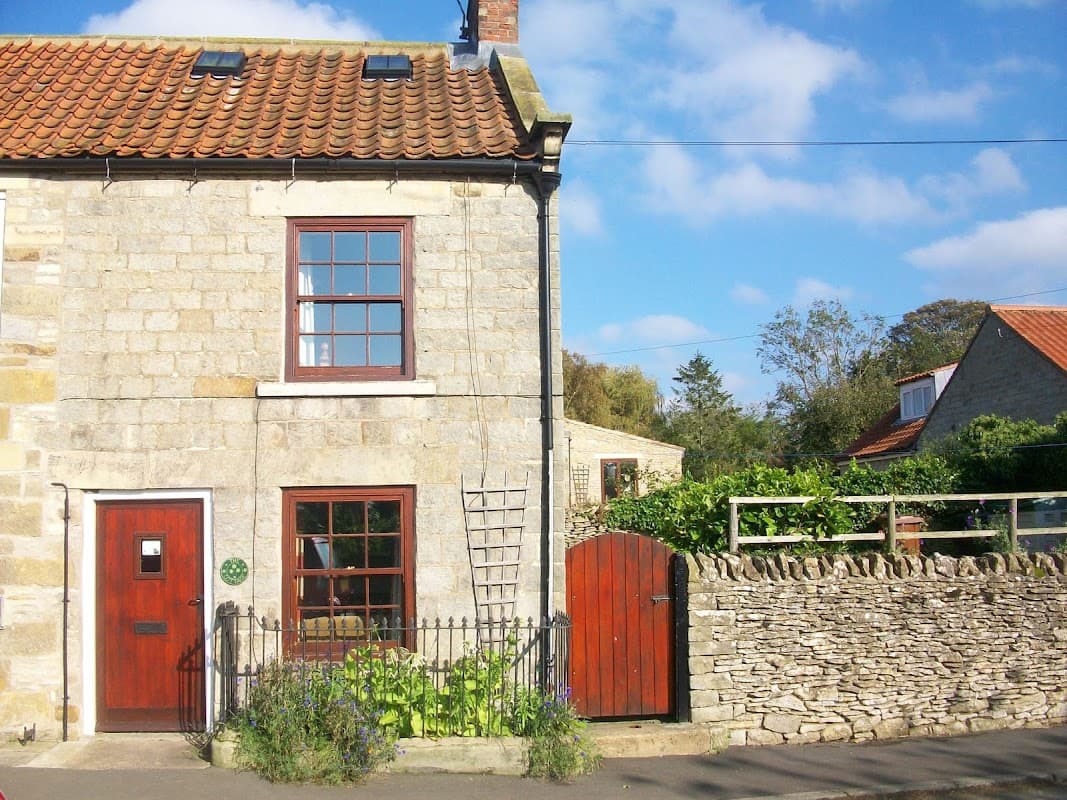 Charming stone cottage with red door, window, and a garden, set against a blue sky in Gillamoor, Yorkshire.