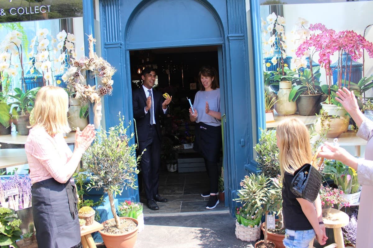 Floral shop entrance with staff and customers, surrounded by plants and flowers, celebrating an event in Gilling West.
