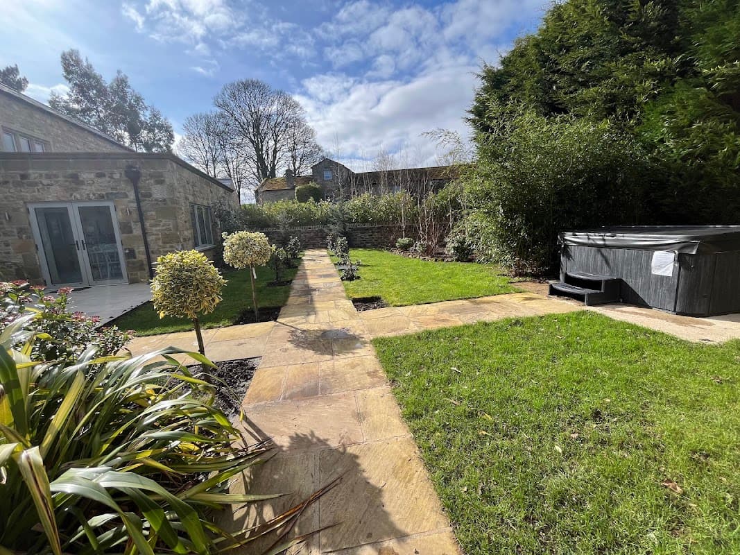 Lush garden with a stone path, hot tub, and greenery surrounding Giling Old Mill Holiday Cottages in Gilling West.