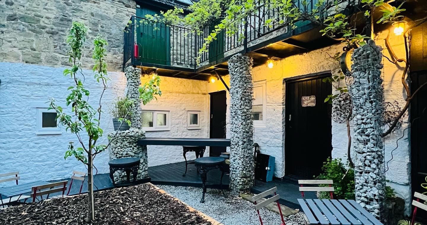 Charming courtyard with stone walls, greenery, outdoor seating, and warm lighting at Stable Yard Rooms in Gilling West.