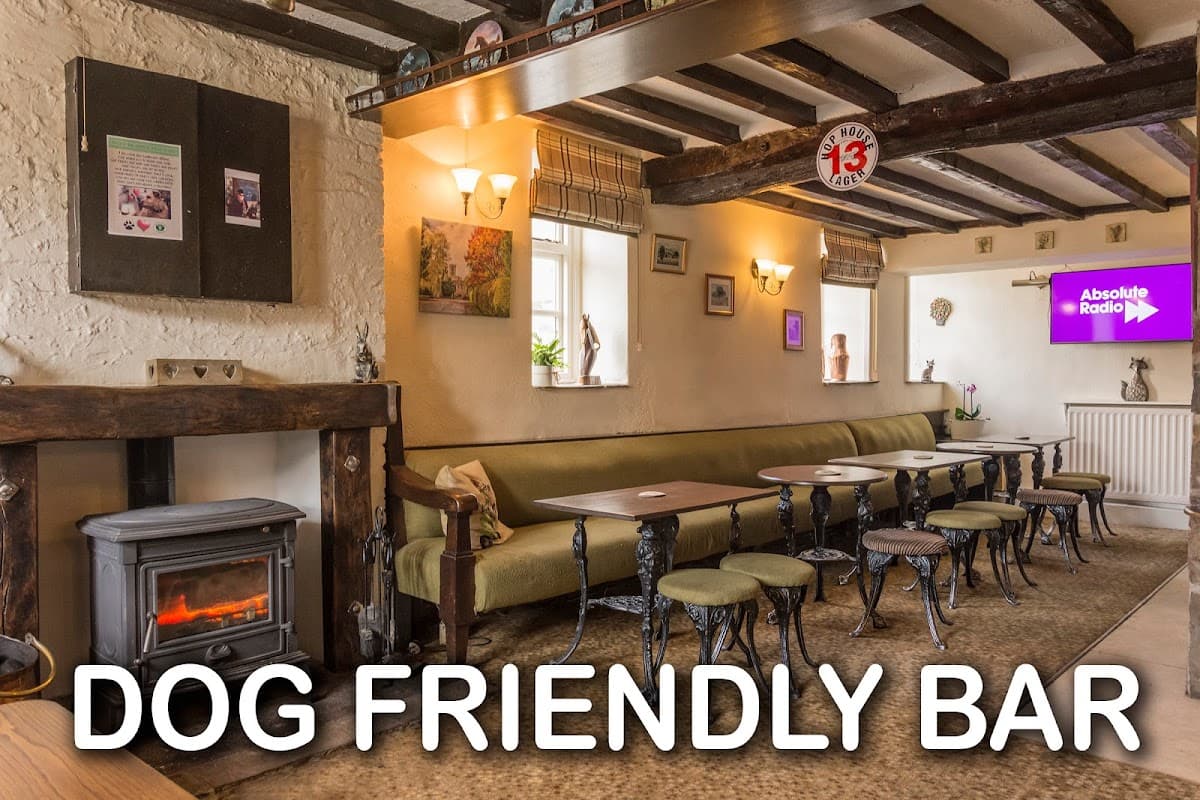 Cozy interior of The Angel Inn with a fireplace, seating, and a TV displaying Absolute Radio, featuring a dog-friendly sign.