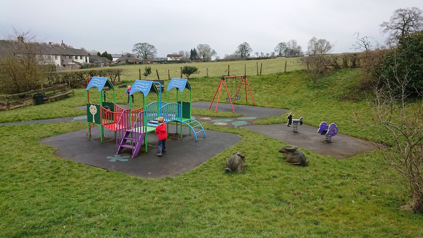 Colorful playground equipment with slides and swings, surrounded by grass and trees in Gisburn, Yorkshire.